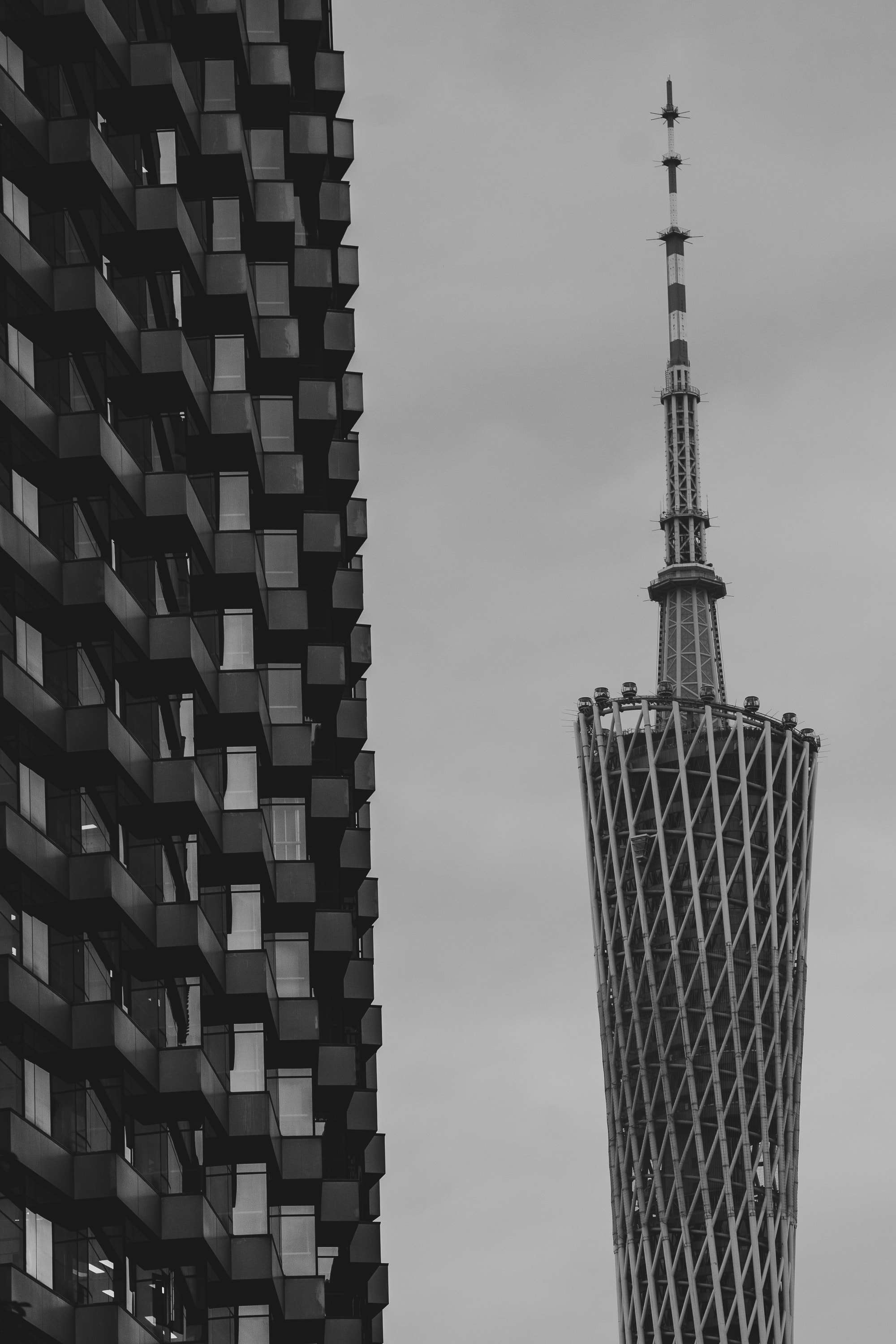 Black and white: the twisted lattice of the Canton Tower and its mast rise beside the stacked, jutting balconies of a residential building.