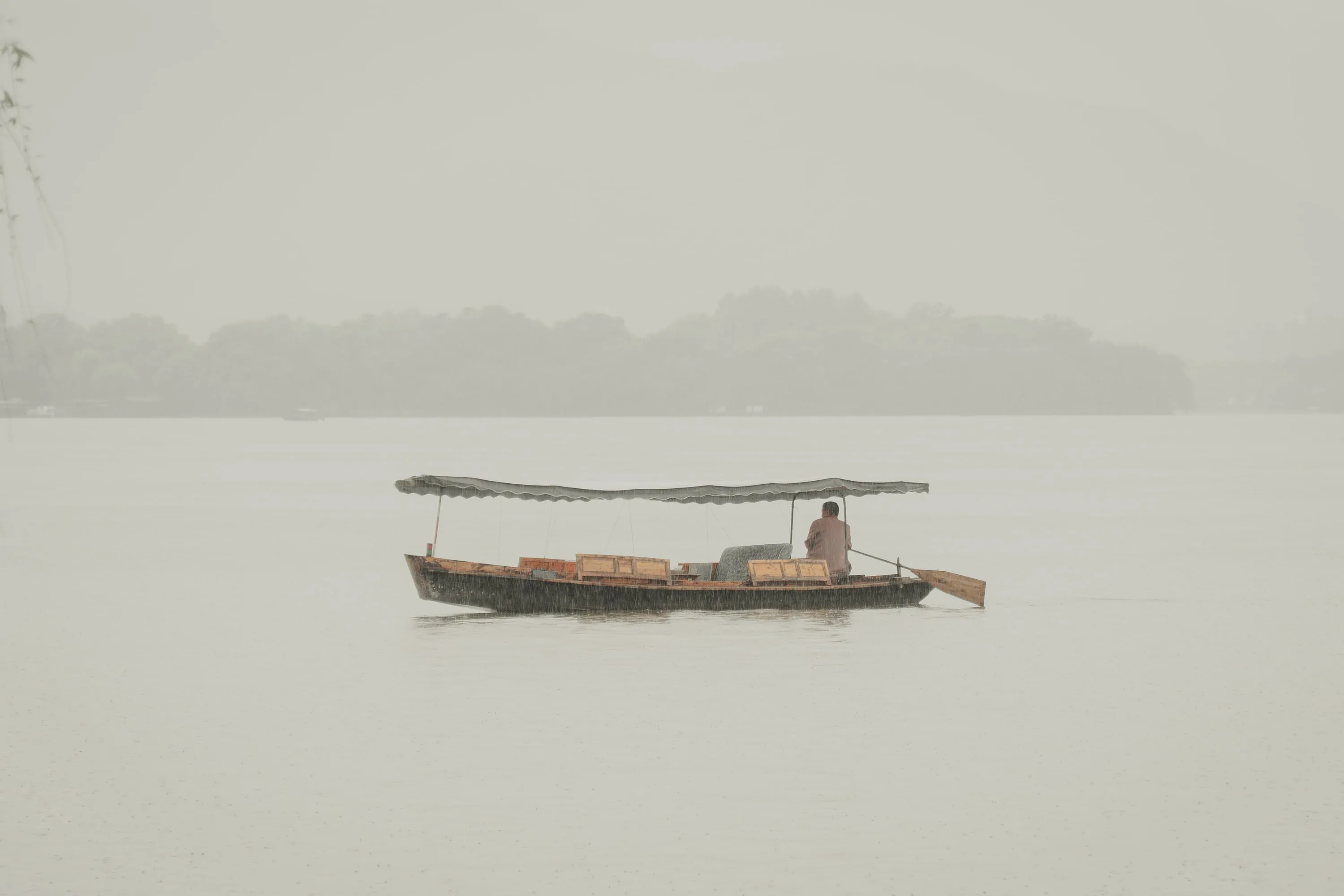 A single covered wooden boat on flat, misty water with a faint tree line behind.