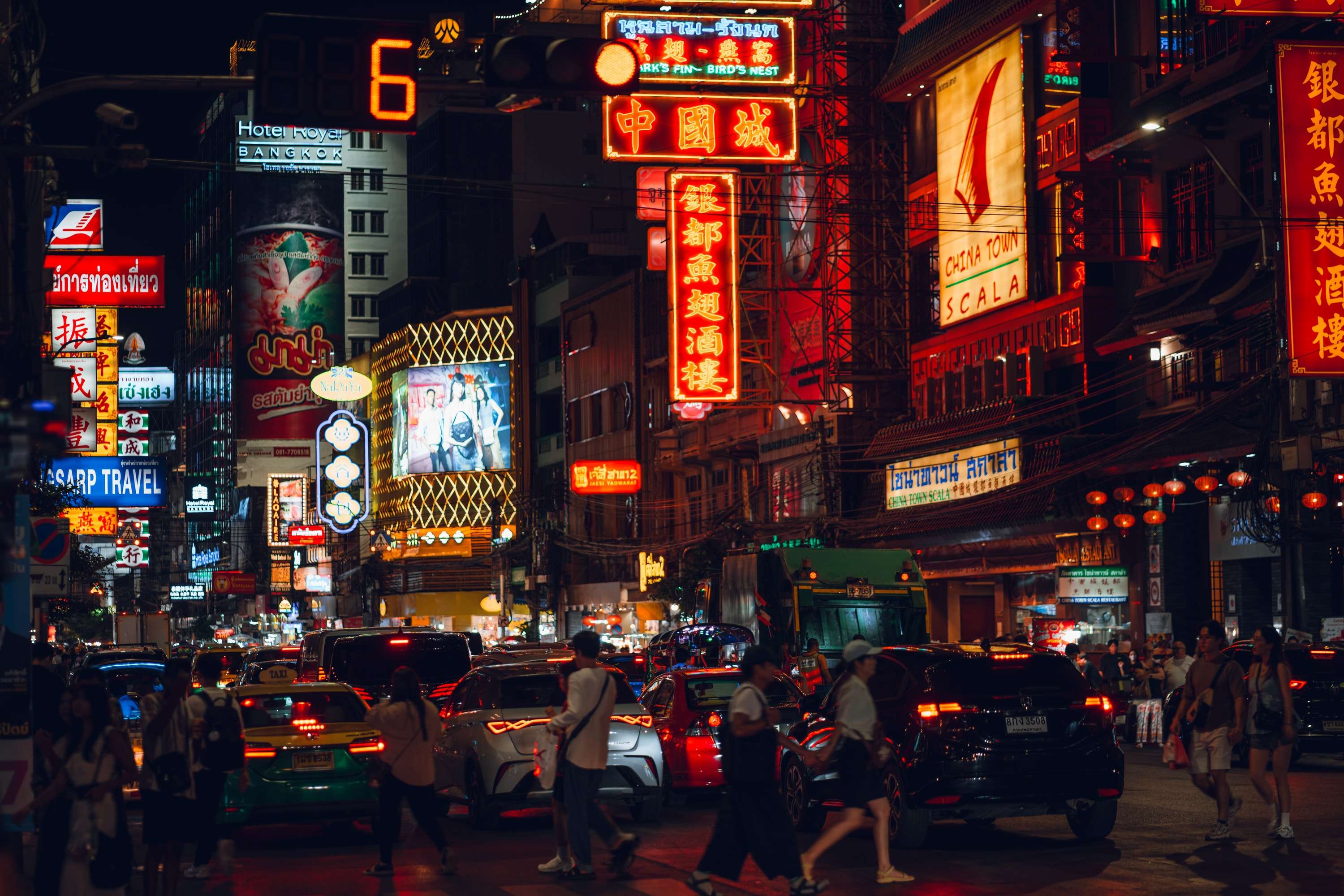 Yaowarat Road at night: red and gold neon signs in Chinese and Thai over a street of slow traffic, with people crossing in front.