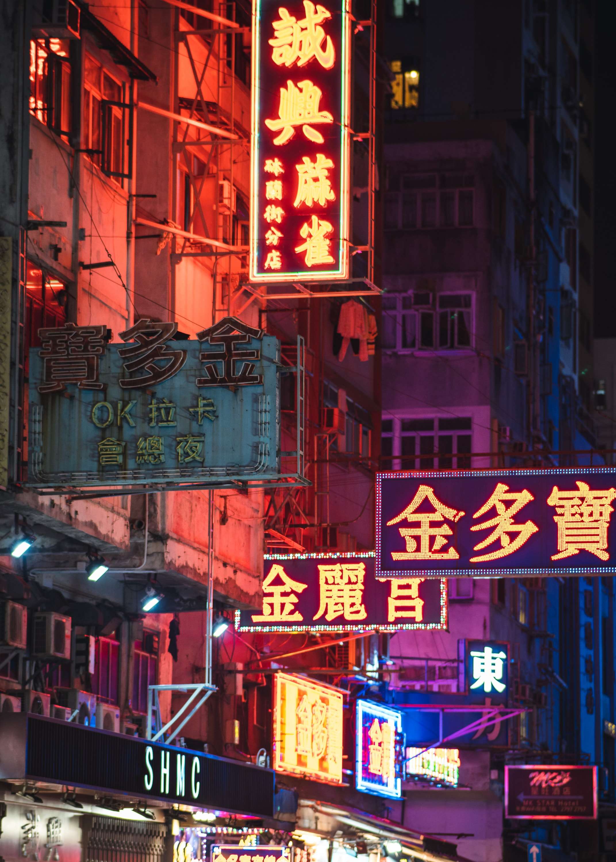 Red, pink and yellow neon signs with Chinese characters stacked above a narrow street at night.