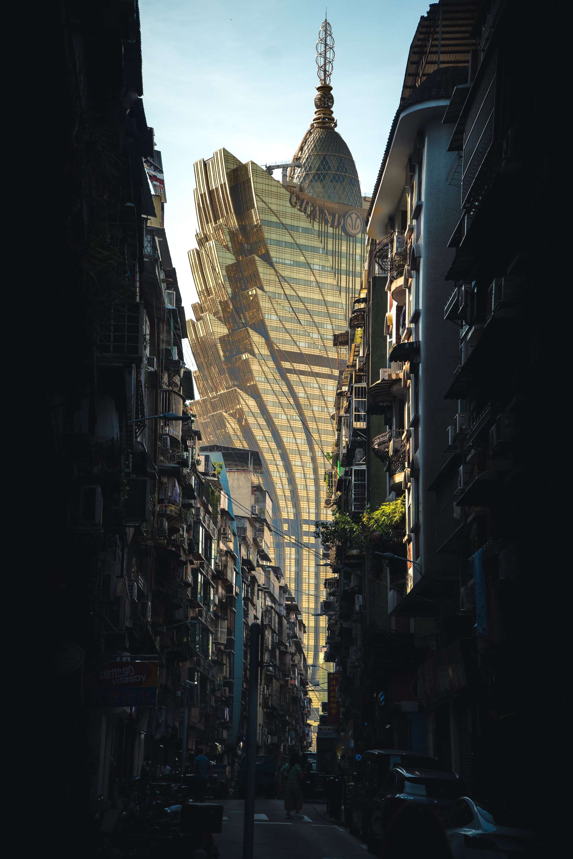 The gold, feather-shaped tower of the Grand Lisboa rises at the end of a narrow street between dark, cluttered apartment blocks.
