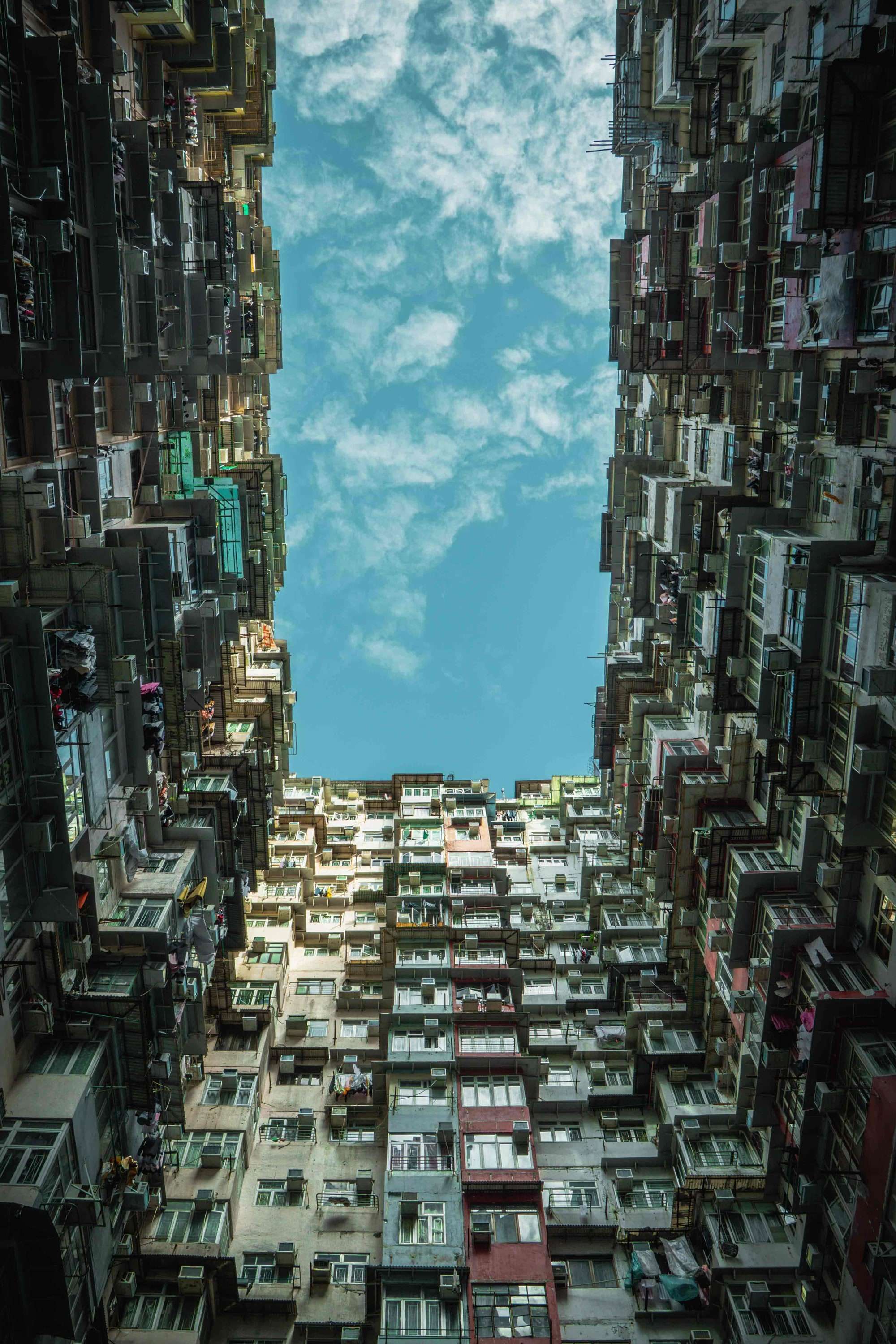 Looking straight up between the stacked apartment blocks of the Yik Cheong Building towards a strip of blue sky and cloud.