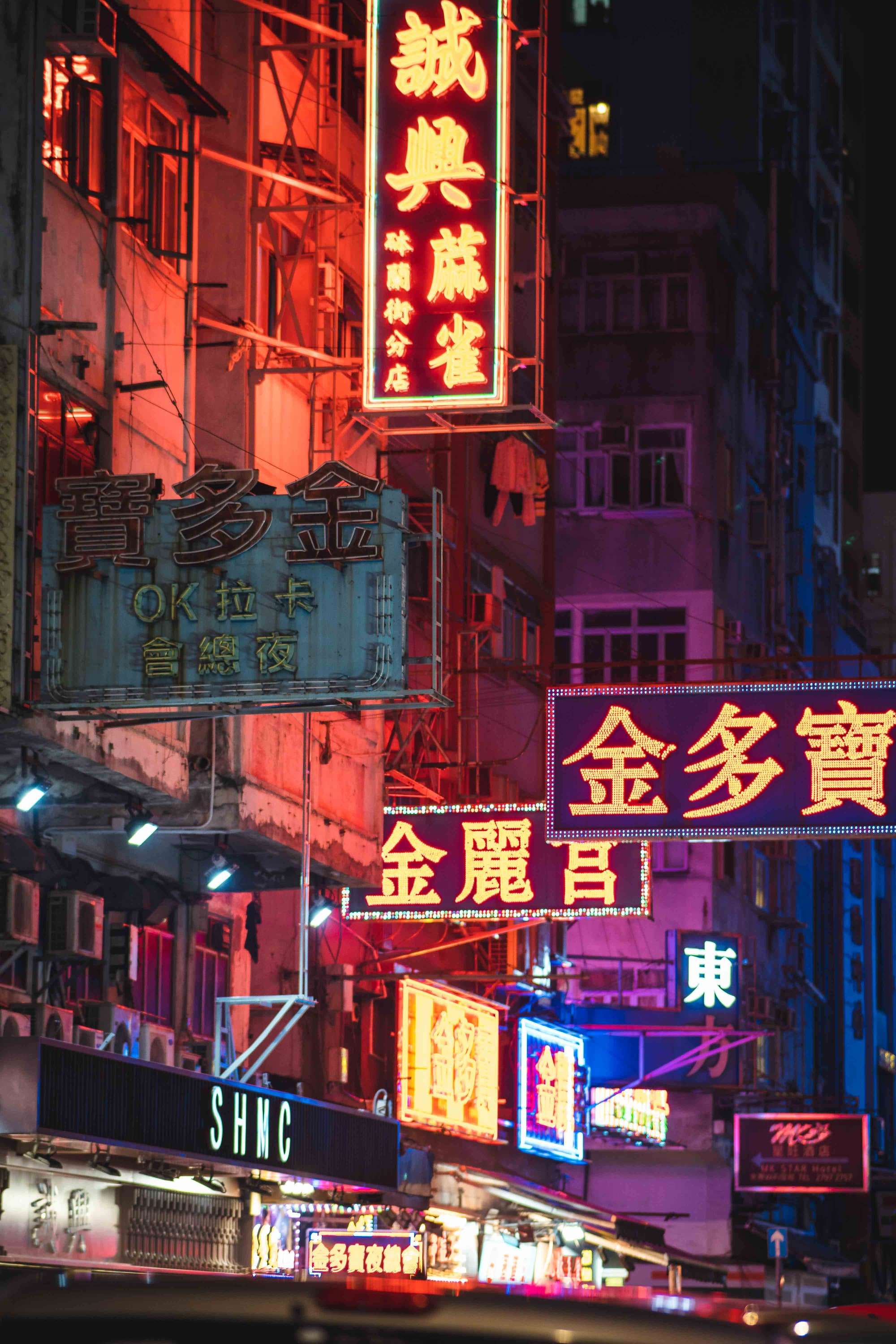 Red, pink and yellow neon signs with Chinese characters stacked above a narrow street at night.